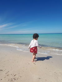 Girl walking at beach against blue sky