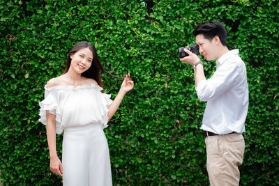 Young woman photographing with camera while standing by plants