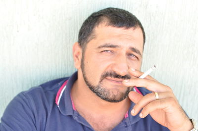 Portrait of man smoking cigarette against wall