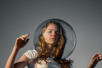 Low angle portrait of young woman wearing glass helmet in head against gray background