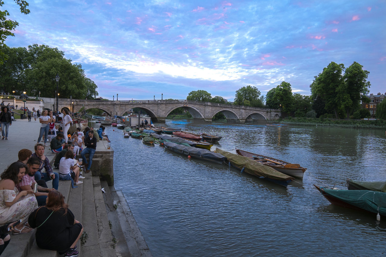 PEOPLE ON RIVER BY BRIDGE AGAINST SKY