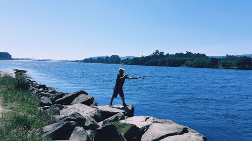 Man standing on rock by lake against sky