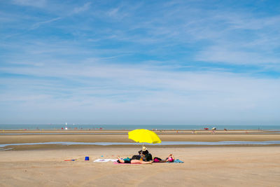 People relaxing below yellow umbrella at beach