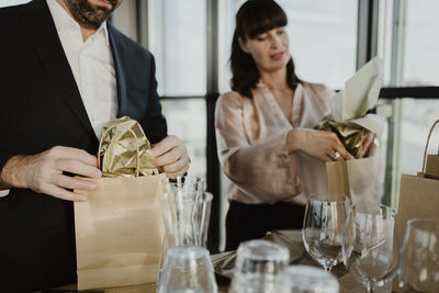 Male and female colleagues putting gifts in paper bag at office party