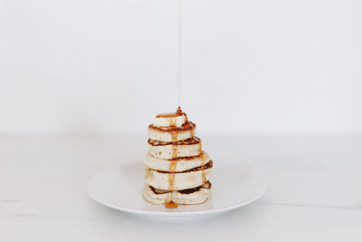 Syrup being poured on a stack of pancakes in a white kitchen scene.