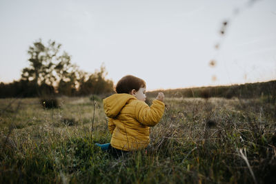 Rear view of boy sitting on grass against sky