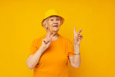 Young woman gesturing against yellow background