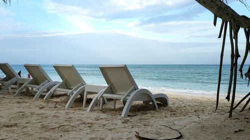 Empty chairs on beach against sky