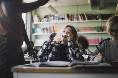 Boy showing paper chit to teacher while copying in classroom