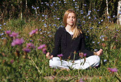 Woman with eyes closed doing yoga amidst flowers on field