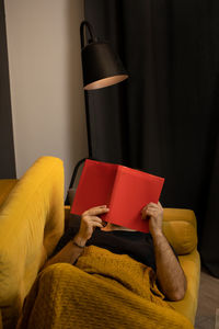 Man reading book while lying on sofa at home