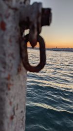 Close-up of metal railing against sea during sunset