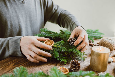 A man makes a christmas decoration for his home from fresh spruce branches and dried orange slices. 