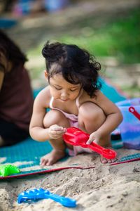 Cute girl playing with toys while crouching on sand