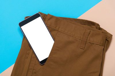 Directly above view of smart phone in brown pant pocket against colored background