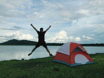 Man with arms raised on field against sky