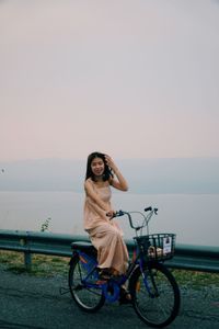 Portrait of woman with bicycle against sky