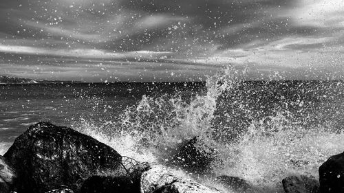 Water splashing on rocks against sky