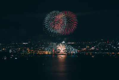 Firework display over illuminated city against sky at night