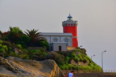 View of lighthouse by building against sky