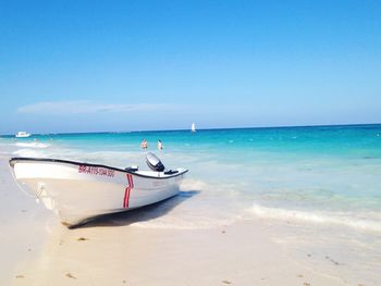 Boat moored on beach against clear blue sky