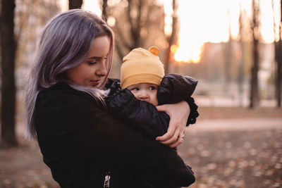 Young mother holding cute baby son in park during autumn at sunset