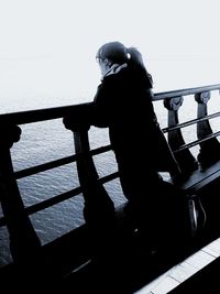 Man sitting on railing by sea against sky