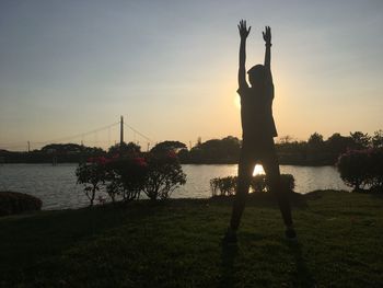 Silhouette person standing by lake against sky during sunset