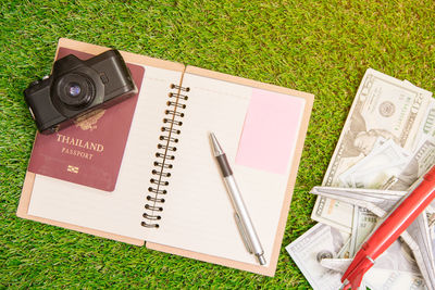 High angle view of book with camera and paper currencies on field