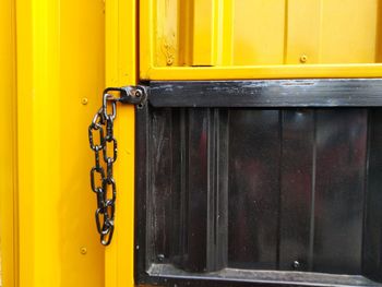 Close-up of metal chain hanging on yellow door