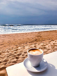 Coffee cup on table by sea against sky