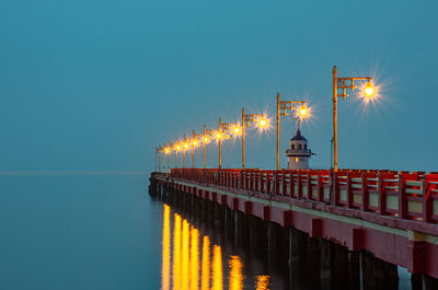 Illuminated street light on bridge over sea against clear sky at night