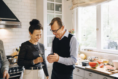 Smiling man and woman sharing smart phone while standing in kitchen