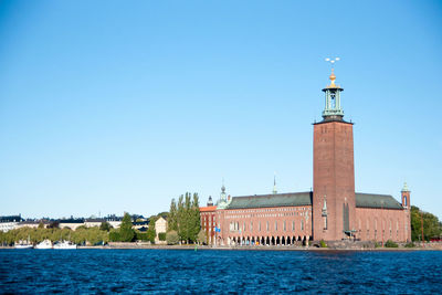 Lighthouse on building by sea against clear blue sky