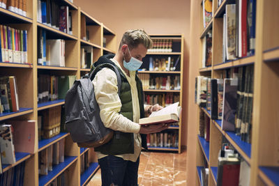 Young man with a mask is reading books in the university library