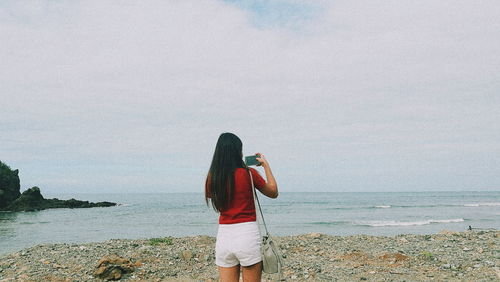 Rear view of woman photographing sea against sky