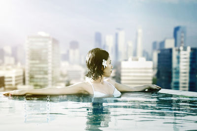 Woman relaxing in swimming pool against cityscape