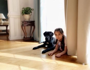 Portrait of girl with dog sitting on hardwood floor at home
