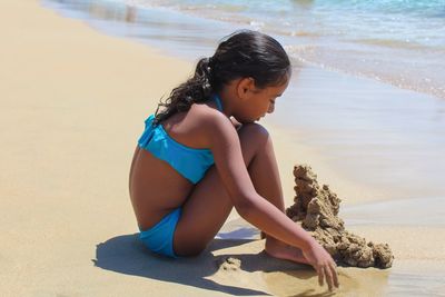 Side view of girl playing with sand at beach on sunny day