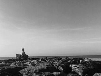 Woman standing on rock by sea against sky