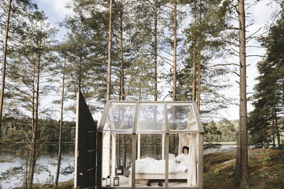 Young woman working remotely on laptop in glass cottage during vacation