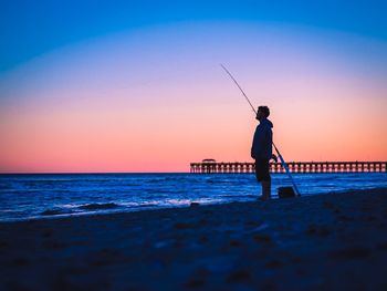 Surface level view of silhouette man fishing on shore against clear sky