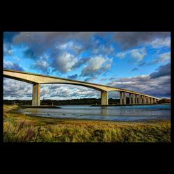 Bridge over river against cloudy sky