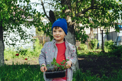 Smiling child holding bell pepper seedlings in hands. happy girl helps family in vegetable garden. 