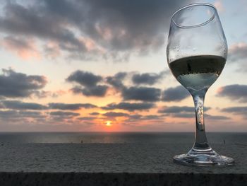 Close-up of beer in sea against sunset sky