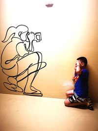 Side view of boy sitting against wall