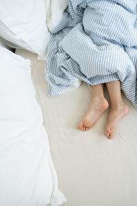 Legs of girl under duvet on bed at home