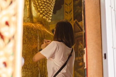 Rear view of woman working on buddha statue at temple