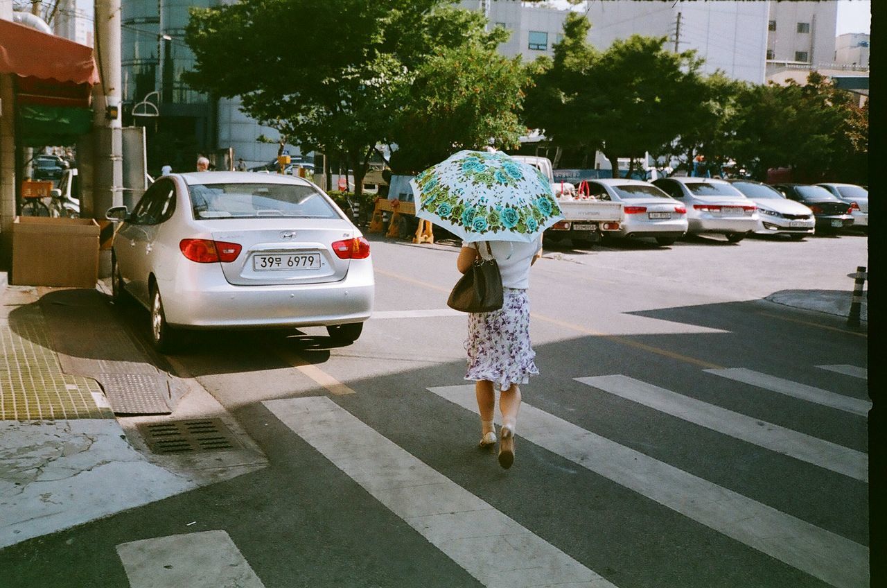 street, full length, lifestyles, walking, casual clothing, rear view, sidewalk, car, city, building exterior, leisure activity, road, city life, transportation, person, land vehicle, day, childhood