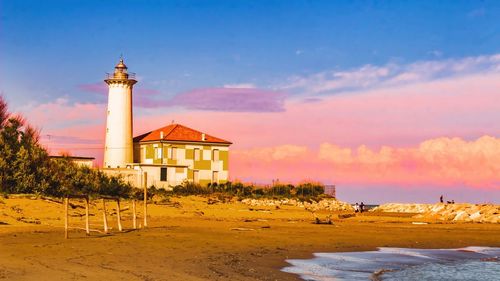 Lighthouse on beach by buildings against sky